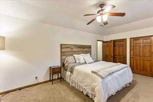 Carpeted bedroom with a ceiling fan, multiple closets, a textured ceiling, and lofted ceiling