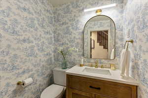 Half bathroom featuring wallpapered walls and vanity