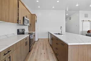 Kitchen with stainless steel appliances, light stone counters, light wood-type flooring, brown cabinets, and recessed lighting