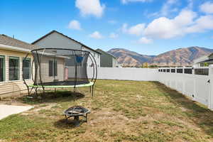 Fenced backyard featuring a trampoline, a fire pit, a mountain view, and a patio