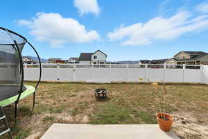 Fenced backyard with a residential view, a trampoline, and an outdoor fire pit