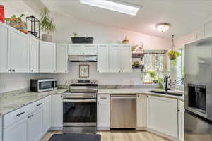 Kitchen featuring appliances with stainless steel finishes, white cabinets, vaulted ceiling, a skylight, and light wood-style floors