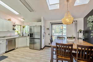 Dining space featuring light wood-style flooring, a chandelier, lofted ceiling, and a skylight