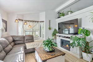 Living area featuring a glass covered fireplace, vaulted ceiling, and light wood-style floors
