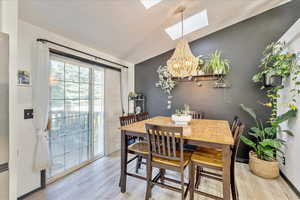 Dining space with vaulted ceiling, light wood-style flooring, a skylight, and a chandelier