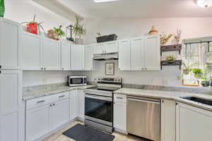 Kitchen featuring stainless steel appliances, white cabinets, light stone counters, and vaulted ceiling