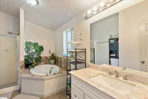 Full bath with a stall shower, a garden tub, vanity, a textured wall, and vaulted ceiling