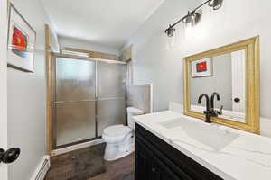 Bathroom with baseboard heating, vanity, a stall shower, and dark wood finished floors