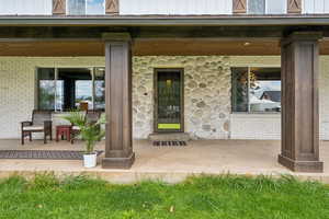 Entrance to property with covered porch, stone siding, and brick siding