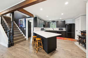 Kitchen featuring black appliances, a peninsula, a breakfast bar, light wood-style flooring, and dark cabinetry