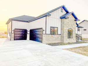 View of front of home featuring driveway, stone siding, a garage, board and batten siding, and roof with shingles