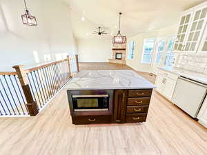 Kitchen featuring light wood-style floors, dark brown cabinetry, open floor plan, pendant lighting, and a stone fireplace