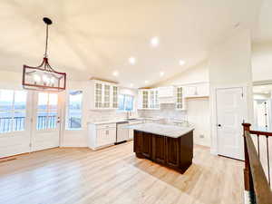 Kitchen with backsplash, lofted ceiling, glass insert cabinets, hanging light fixtures, and a center island
