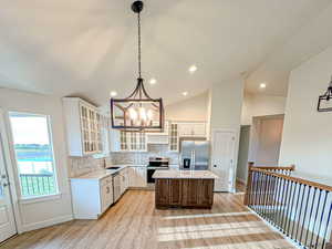 Kitchen with glass insert cabinets, tasteful backsplash, appliances with stainless steel finishes, light wood-style flooring, and vaulted ceiling