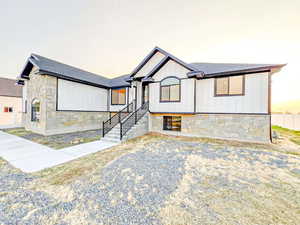 View of front of house with stone siding, roof with shingles, and board and batten siding