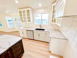 Kitchen with glass insert cabinets, backsplash, light wood finished floors, dishwasher, and light stone countertops