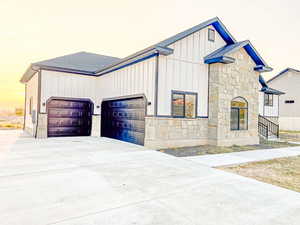 View of front of property featuring concrete driveway, stone siding, a garage, board and batten siding, and roof with shingles