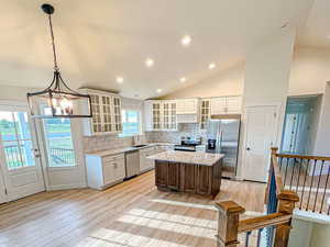 Kitchen with tasteful backsplash, stainless steel appliances, light wood-style flooring, glass insert cabinets, and vaulted ceiling