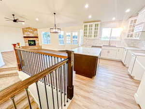Kitchen with decorative backsplash, pendant lighting, white cabinetry, a stone fireplace, and a center island
