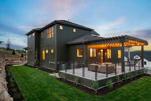 Back of house at dusk with a lawn, board and batten siding, a wooden deck, and a pergola