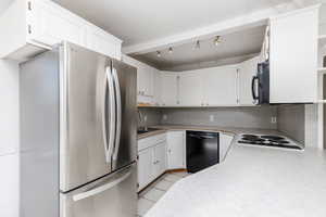 Kitchen featuring white cabinets, black appliances, light countertops, light tile patterned floors, and decorative backsplash