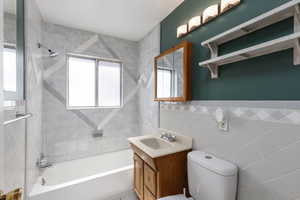 Bathroom with shower / bath combination, vanity, plenty of natural light, and tile walls