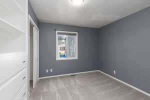 Unfurnished bedroom with light colored carpet, a closet, and a textured ceiling