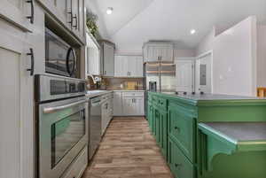 Kitchen featuring stainless steel appliances, green cabinets, decorative backsplash, light wood-type flooring, and vaulted ceiling