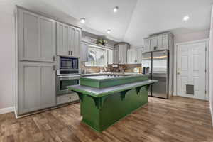 Kitchen featuring vaulted ceiling, a breakfast bar, appliances with stainless steel finishes, backsplash, and a center island