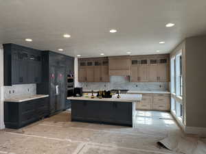 Kitchen featuring a center island, recessed lighting, decorative backsplash, a textured ceiling, and glass insert cabinets