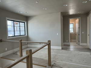 Hallway featuring a textured ceiling, recessed lighting, and an upstairs landing