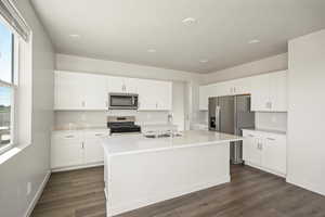 Kitchen featuring white cabinets, appliances with stainless steel finishes, and an island with sink