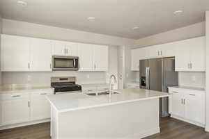 Kitchen featuring appliances with stainless steel finishes, white cabinetry, dark wood-style floors, light stone counters, and a center island with sink