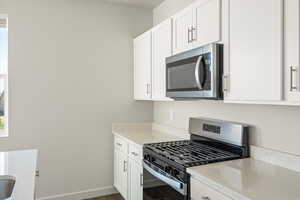 Kitchen featuring appliances with stainless steel finishes, white cabinets, light stone countertops, and dark wood-style flooring