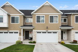 Multi unit property with stone siding, stucco siding, an attached garage, and driveway