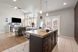Kitchen with a kitchen breakfast bar, pendant lighting, open floor plan, light stone counters, and an island with sink