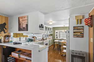 Kitchen with white appliances, heating unit, light wood-style floors, a peninsula, and backsplash
