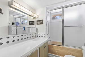 Bathroom with shower / bath combination with glass door, vanity, and decorative backsplash