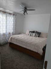 Bedroom with a textured ceiling, carpet, and a ceiling fan