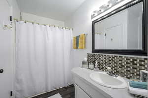 Bathroom featuring vanity, decorative backsplash, and dark wood-style flooring
