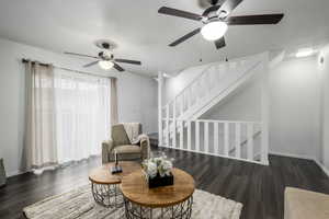 Sitting room featuring dark wood-type flooring, ceiling fan, and stairs