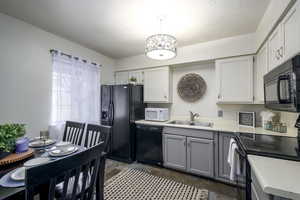 Kitchen featuring gray cabinetry, black appliances, decorative light fixtures, light countertops, and white cabinetry