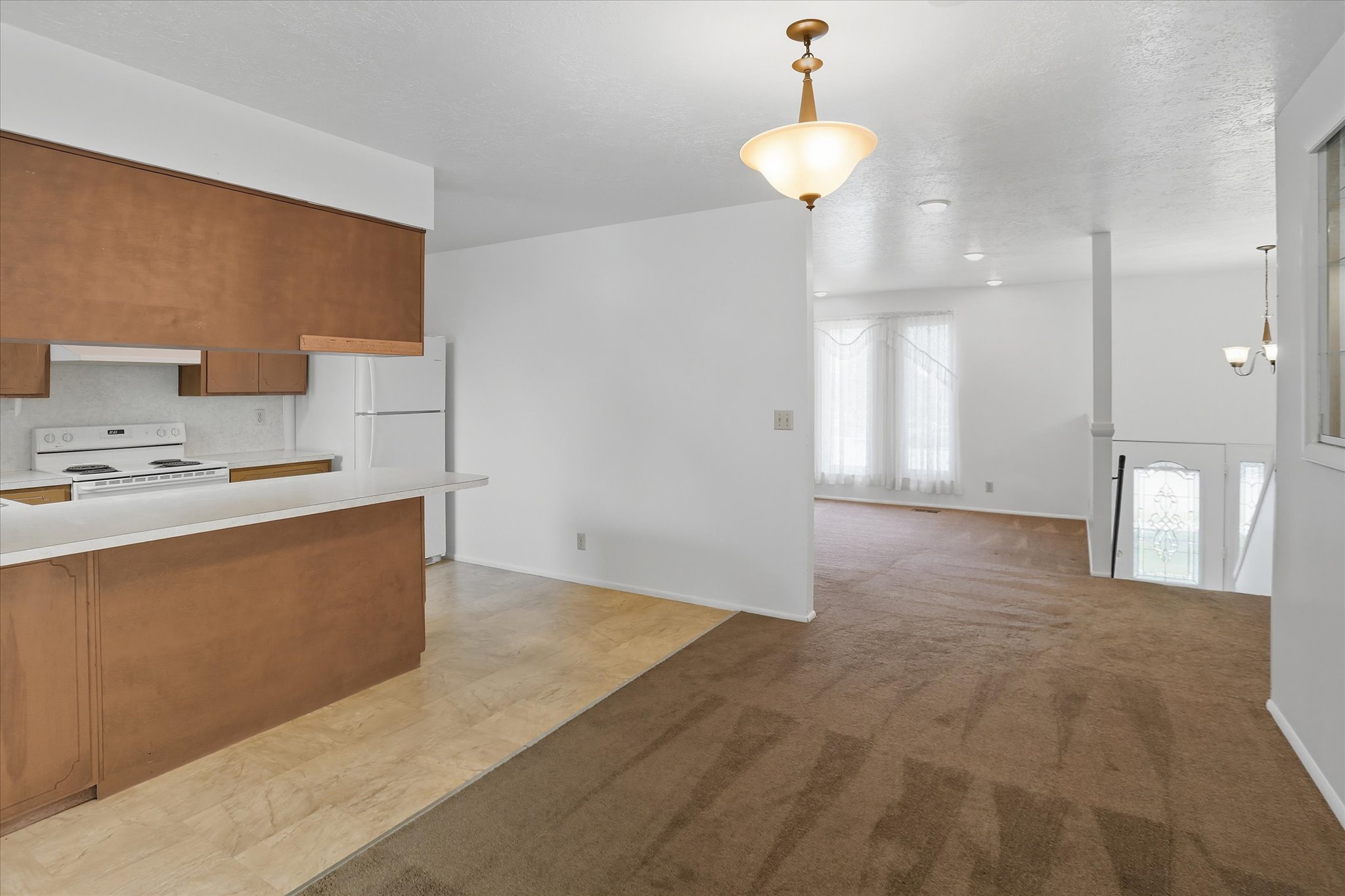 Kitchen with brown cabinets, light countertops, decorative light fixtures, and white appliances