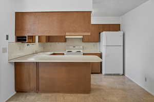Kitchen featuring light countertops, brown cabinets, white appliances, a peninsula