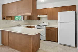 Kitchen featuring white appliances, brown cabinetry, light countertops, a peninsula