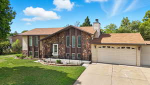 View of front facade featuring stone siding, driveway, roof with shingles, a chimney, and an attached garage