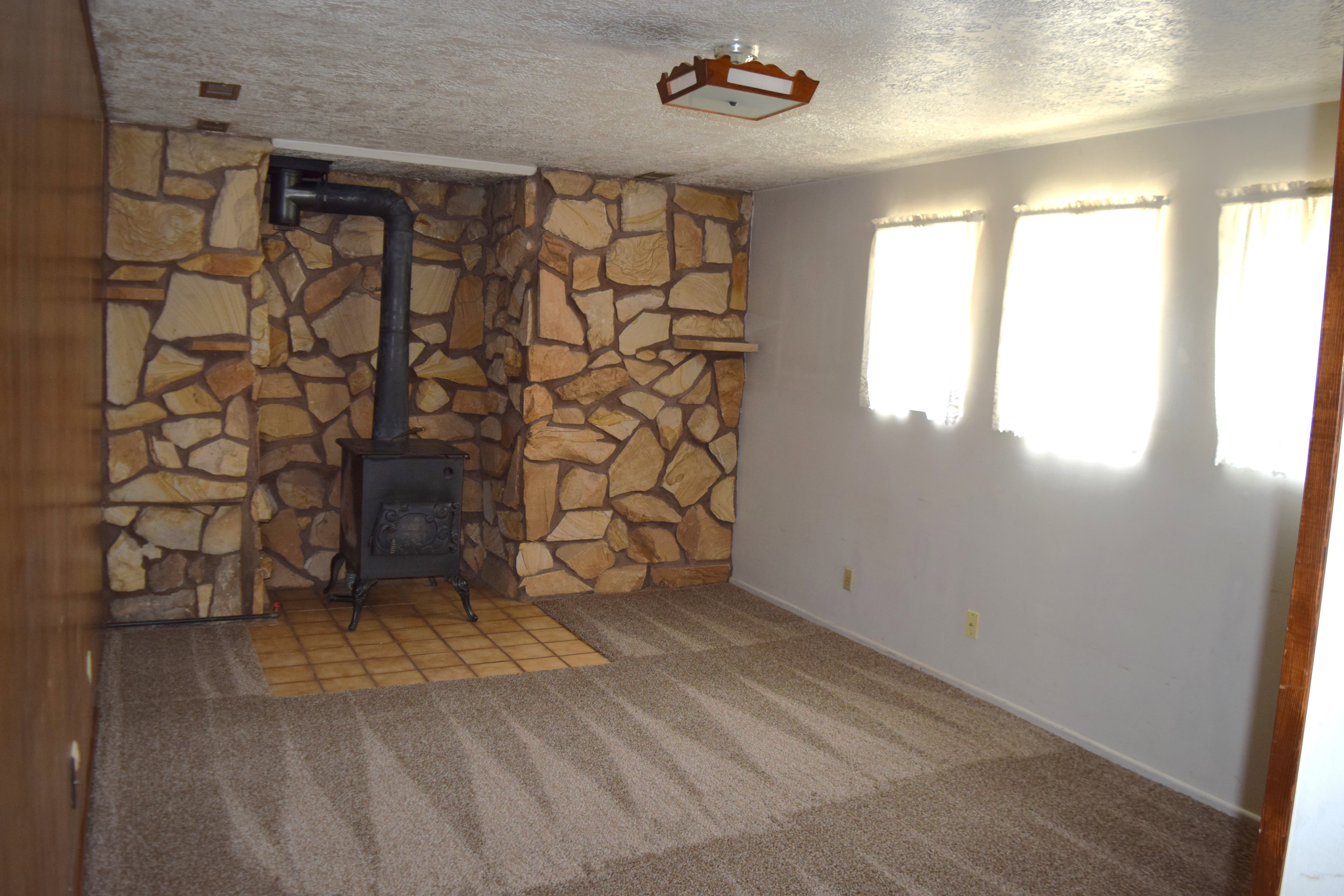 Unfurnished living room featuring light carpet, a textured ceiling, and a wood stove