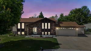 View of front facade featuring stone siding, a front yard, concrete driveway, an attached garage, and a chimney