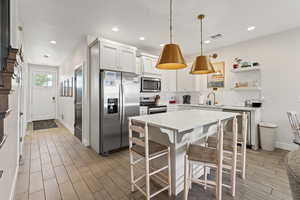 Kitchen with stainless steel appliances, a kitchen bar, tile floors, light cabinets, and decorative light fixtures