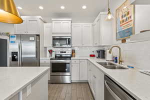 Kitchen with hanging light fixtures, appliances with stainless steel finishes, light quartz counters, backsplash, and recessed lighting